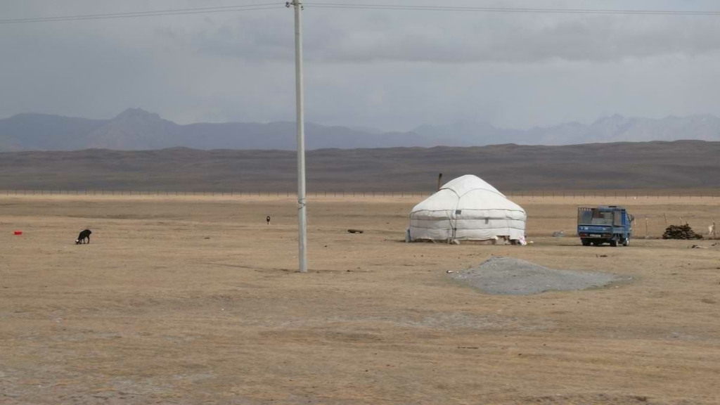 Jurte in Steppe. Pickup rechts daneben. Grasendes Tier links. Im Hintergrnd Gebirge